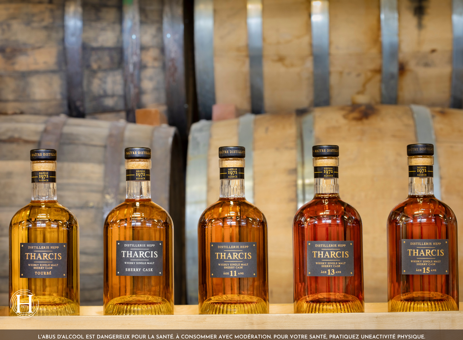 Les cinq whiskies alsaciens Tharcis de la Distillerie HEPP devant les fûts